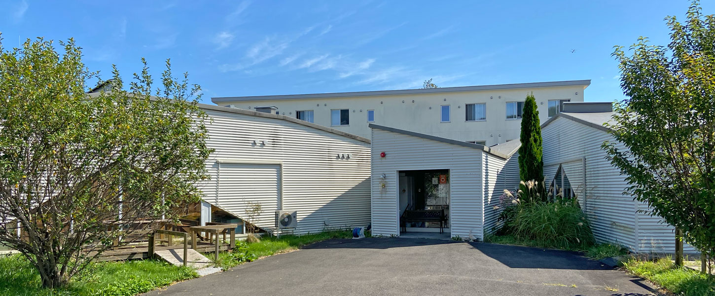 介護施設の建物外観。白い外壁で複層構造、正面に入口が見える。